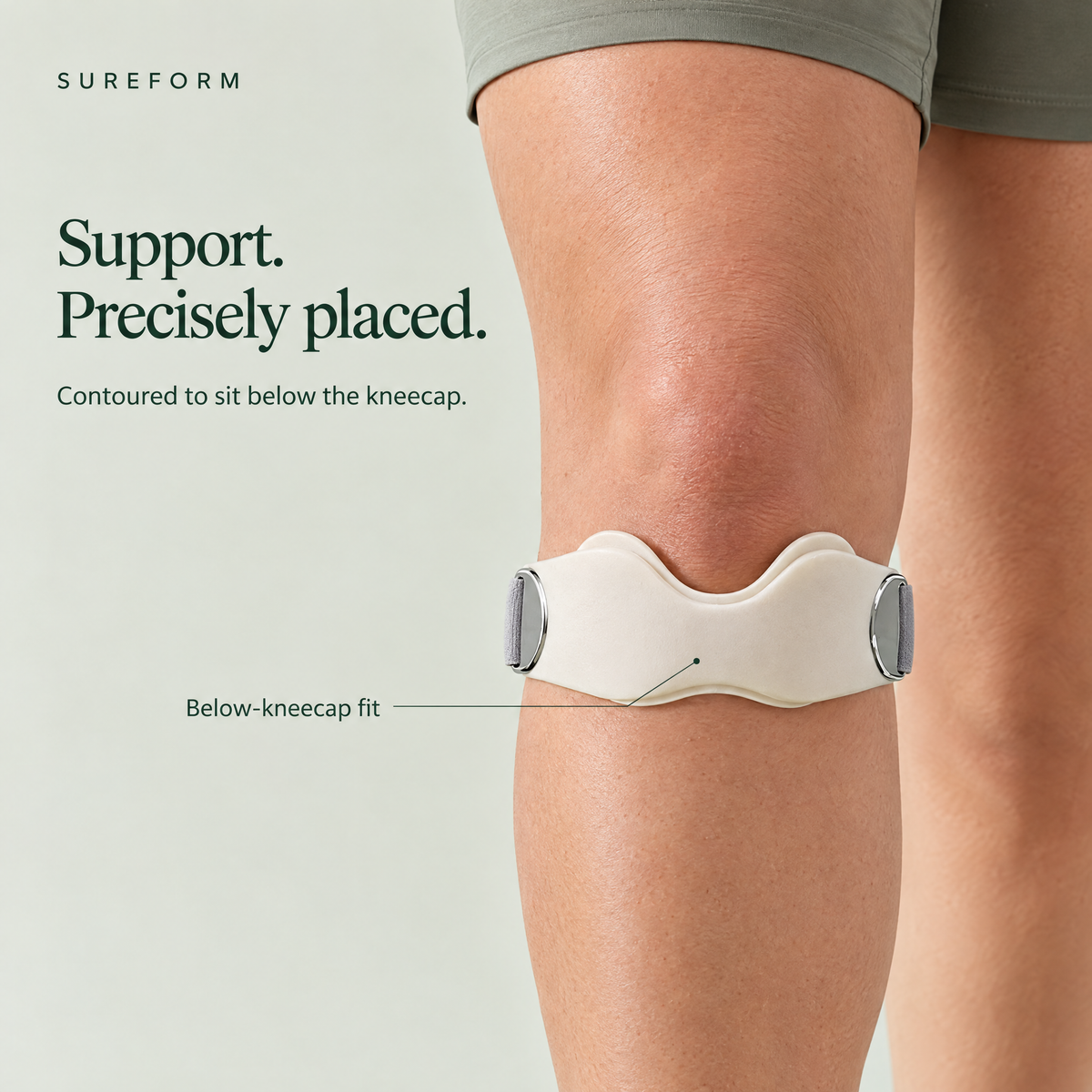 SureForm off-white tendon support strap centered below the kneecap, with the curved dip upright and silver buckles at both sides.